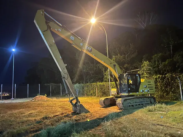 Escavadeira de longo alcance Caterpillar em obra à noite
