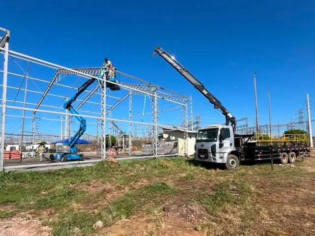 Caminhão munck da SL com a lança estendida em içamento numa obra de estrutura metálica